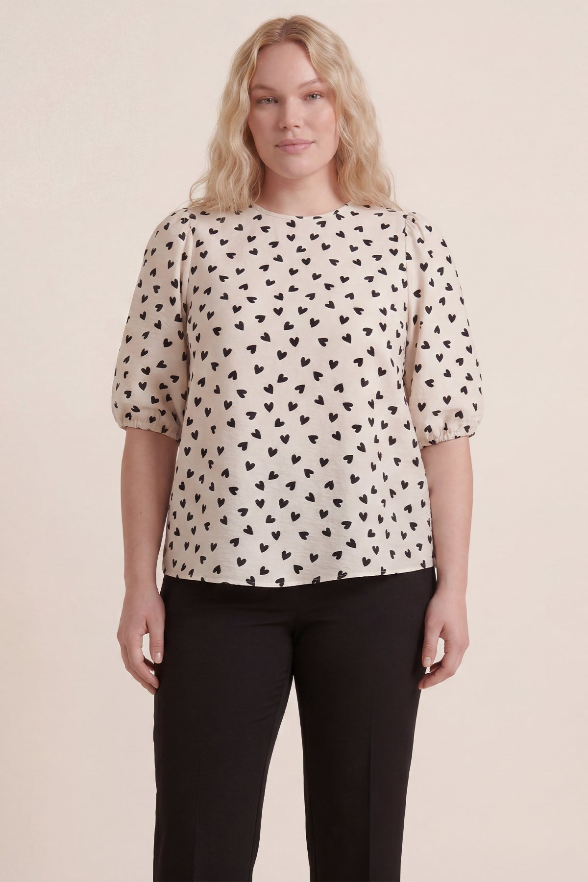Plus-size woman in cream heart-print top and black pants, perfect for big size office fashion.